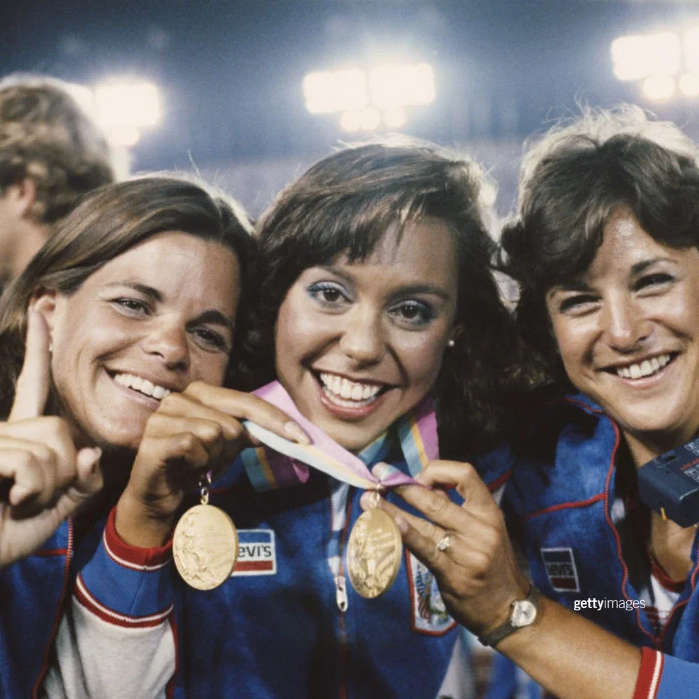 Tracie Ruiz holding her gold medal around her neck flanked by her coaches at the 1984 Games Closing Ceremonies.