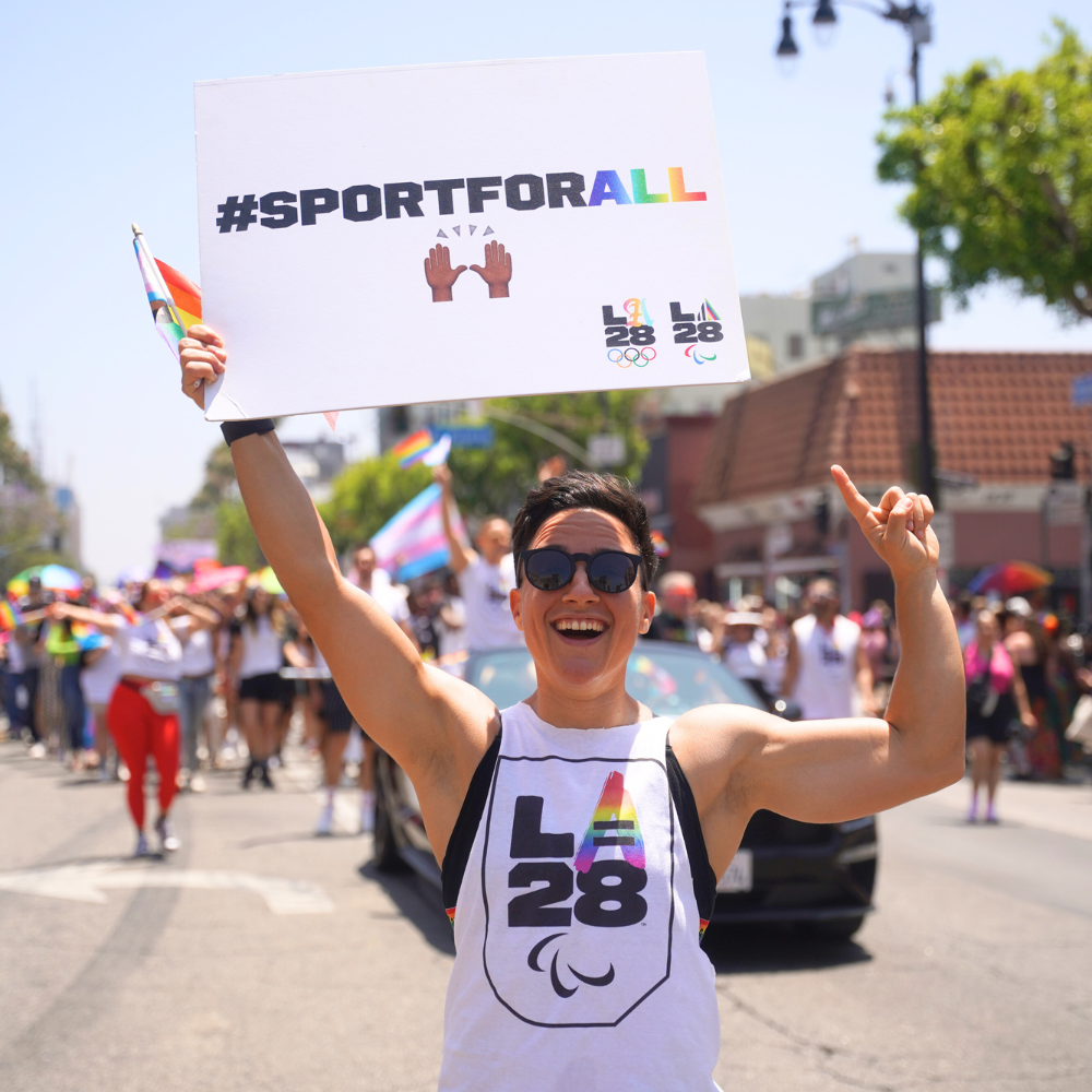 Izzy at the LA Pride Parade holding a sign that says 'sport for all'