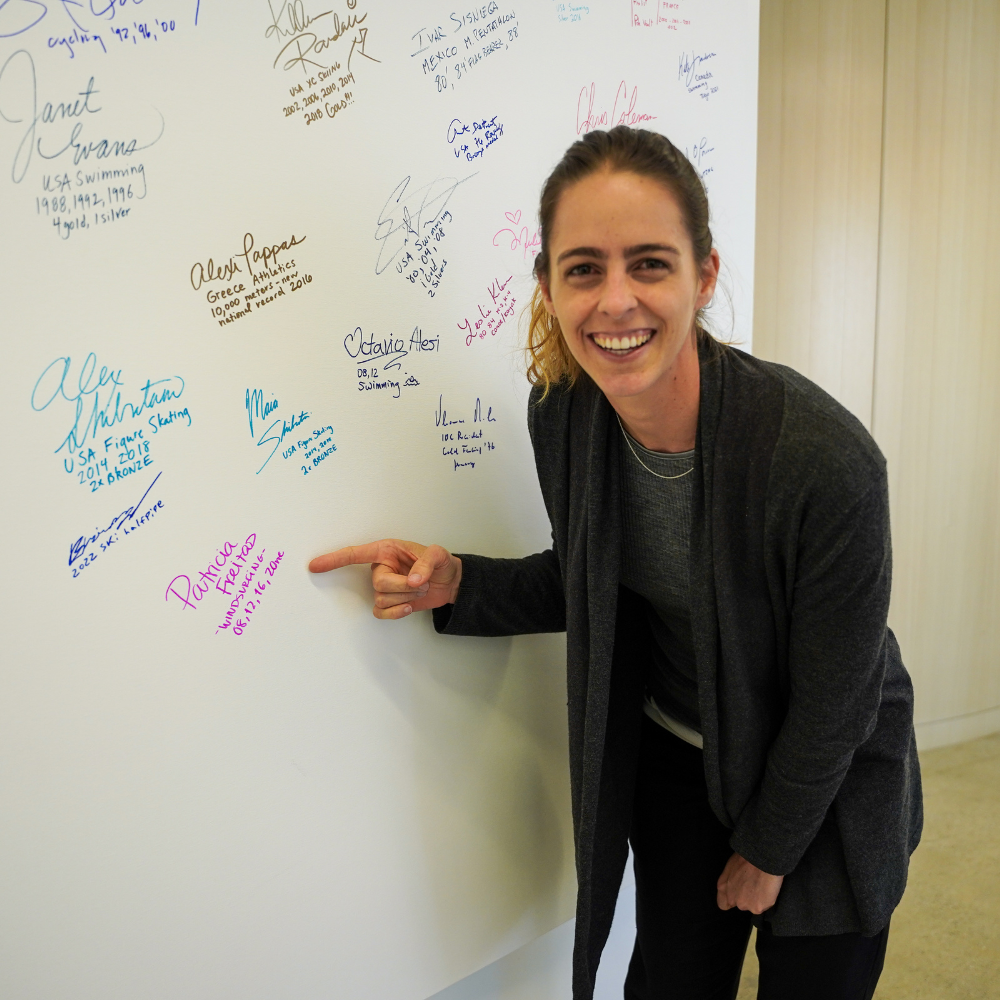 Picture of Patricia smiling next to her signature on the Olympian and Paralympian wall at LA28 offices