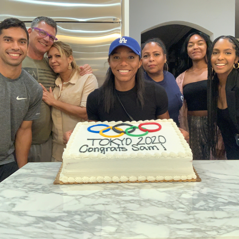 Sam Dirks surrounded by her family members smiling and holding a cake that says 'Tokyo 2020' with the Olympic rings