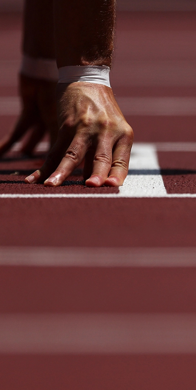 Runner's hands on the starting line of a track with white tape wrapped around some fingers