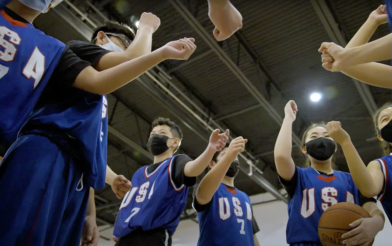 A group of young athletes in blue basketball jerseys that say USA with their hands in the air