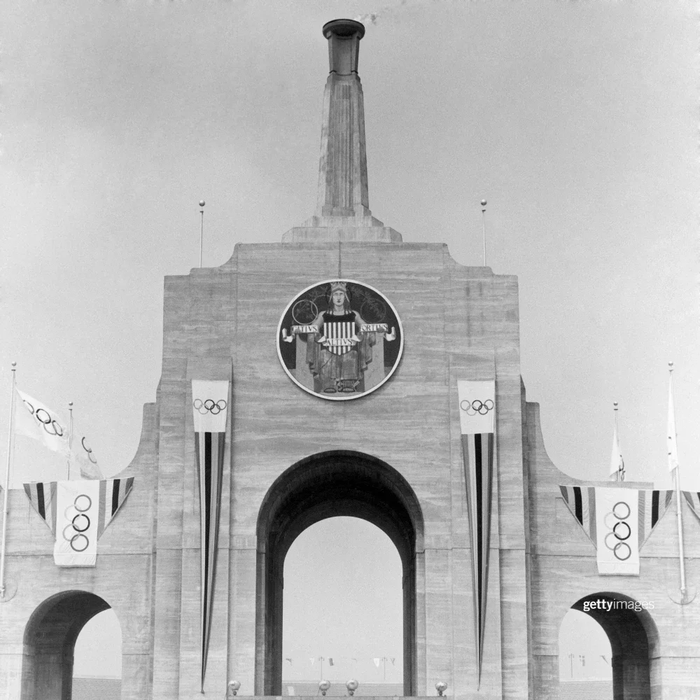 Foto en blanco y negro del Coliseo Memorial de Los Ángeles con el pebetero olímpico encendido y ocho banderas olímpicas durante los Juegos de 1932