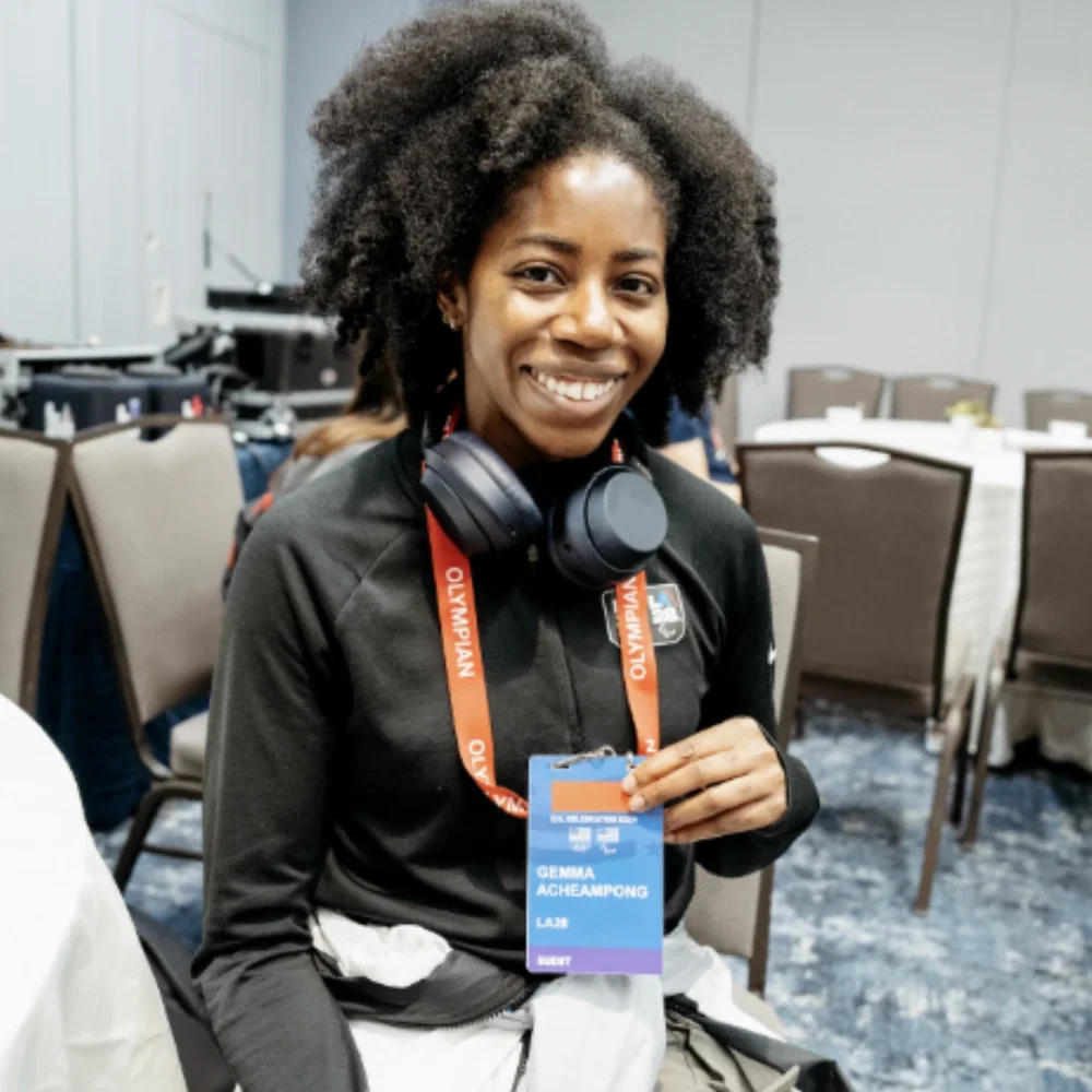 Gemma Acheampong smiling and sitting while holding up a lanyard 