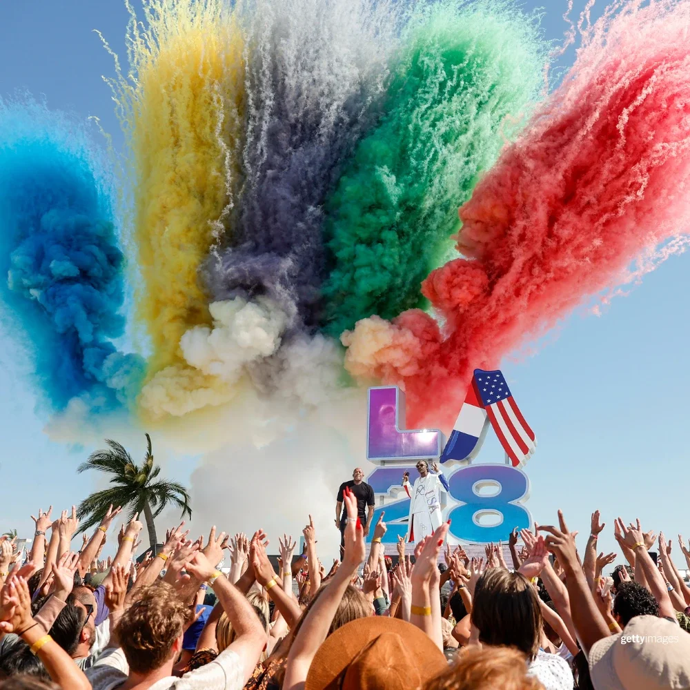 Foto de humo de colores en negro, azul, rojo, amarillo y verde frente a un escenario con Dr. Dre y Snoop Dogg cantando en la ceremonia de presentación del Handover olímpico LA28.