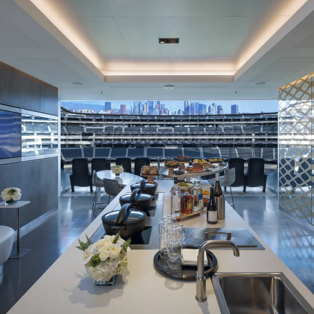 A hospitality suite with a food setup inside the suite. An island with a sink and dark wood cabinetry is shown in the foreground.
