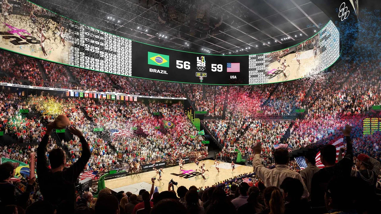 Una representación digital muestra un concurrido partido de baloncesto en Intuit Dome. El marcador muestra USA 59 y Brasil 56, y las grandes pantallas digitales que rodean la cancha muestran la acción del juego. El estadio está lleno de aficionados emocionados con banderas de varios países. La cancha tiene el logotipo de LA28, indicando que es un juego olímpico. Hay muchas luces coloridas y confeti en la escena.