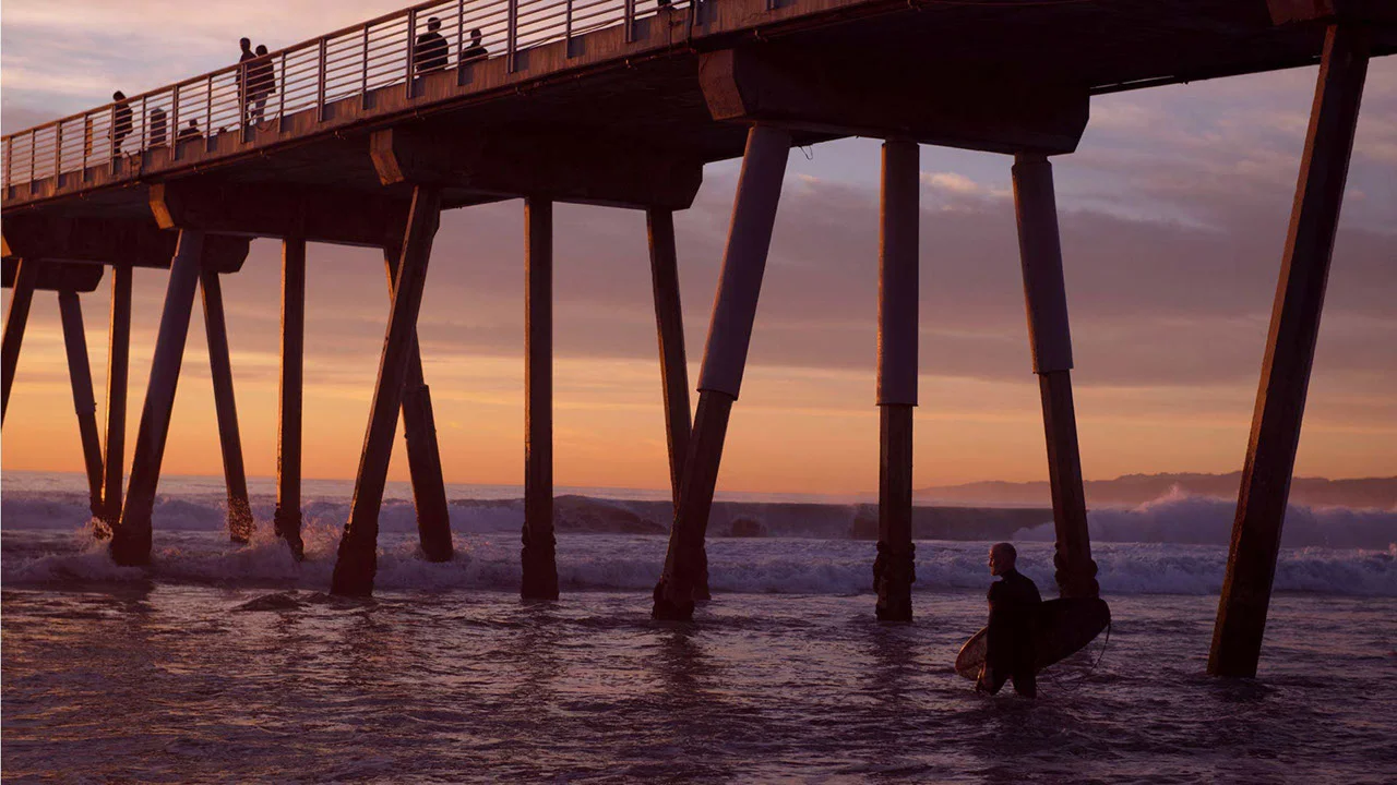 Fotografía mostrando uno de los muelles en Los Ángeles con un surfer en el primer plano. 