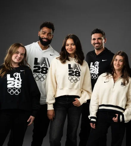 Miembros del programa de Atletas LA28 vistiendo diversas prendas LA28 x Nike, incluyendo camisetas y sudaderas con capucha en los colores crema, negro y blanco