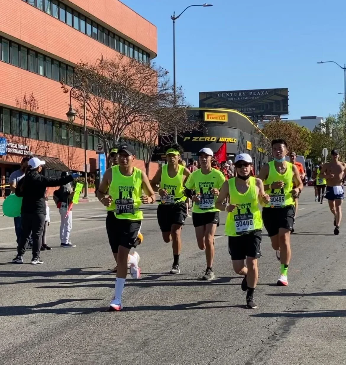 A group of runners on the street wearing hats and neon green shirts that say Students Run LA