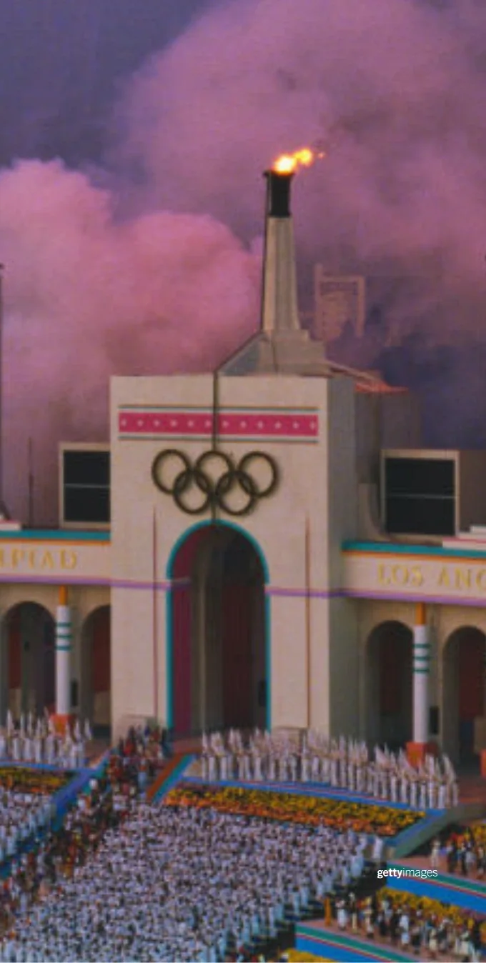 Una fotografía del Coliseo durante la Ceremonia de Clausura de los Juegos de Los Ángeles 1984. La imagen muestra el Coliseo y dos pantallas, con la pantalla izquierda mostrando las palabras: 'Buena suerte a los atletas del mundo'.