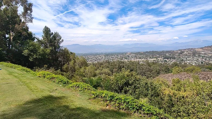 Una fotografía del Industry Hills MTB Course, con pasto en primer plano y árboles con las montañas de San Gabriel al fondo.