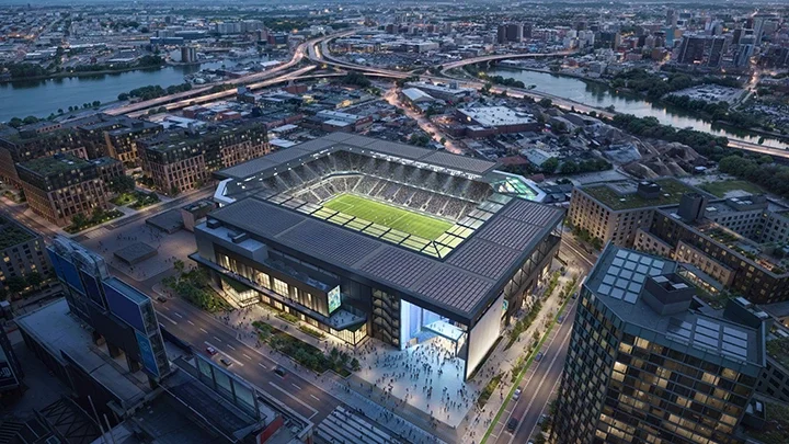 Renderización del New York Stadium, conocido como Etihad Park, que muestra el estadio de fútbol desde una vista aérea, con edificios urbanos y calles de la ciudad alrededor del recinto. En primer plano se ven aficionados entrando al estadio.
