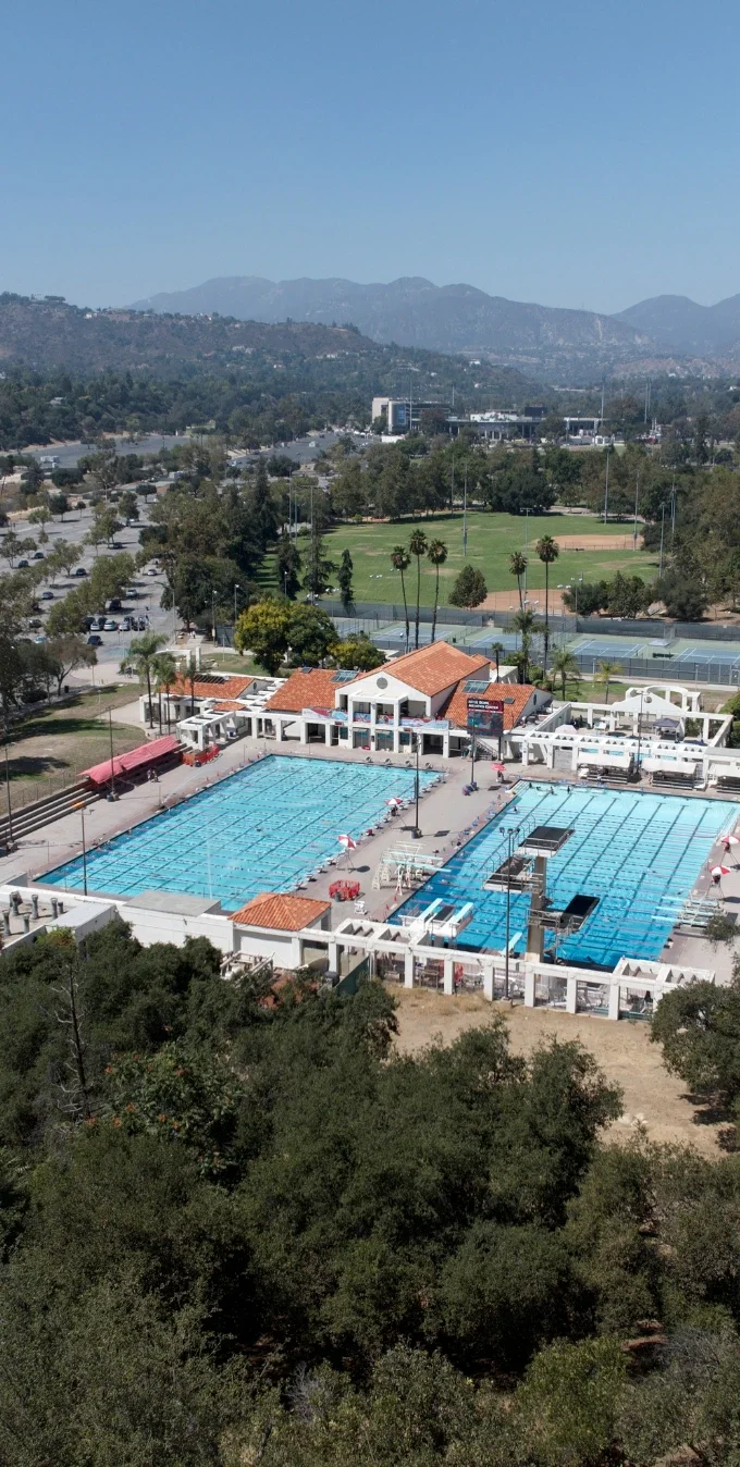 Fotografía aérea del Rose Bowl Aquatics Center que muestra una piscina en el centro, rodeada de árboles y las laderas del cañón Arroyo Seco alrededor del centro acuático.