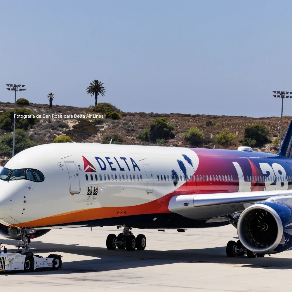 Imagen de un avión de Delta con el diseño de LA28, con el morro en ángulo sobre la pista y los acantilados de El Segundo al fondo.