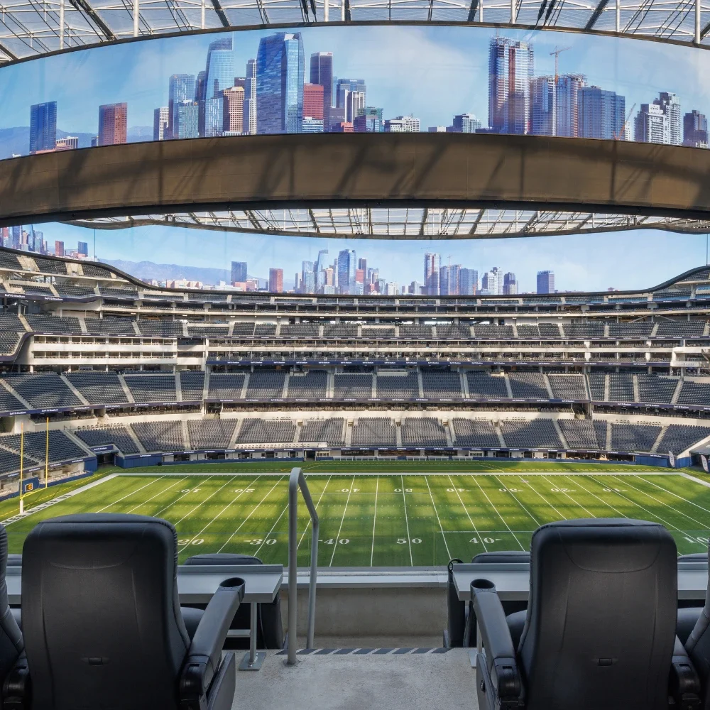 Vista desde un suite con asientos premium negros en primer plano y vista al campo de fútbol americano en el SoFi Stadium
