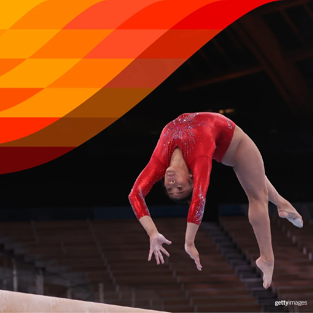 Fotografía de una gimnasta femenina con un leotardo rojo realizando un salto hacia atrás sobre la viga, capturada en el aire