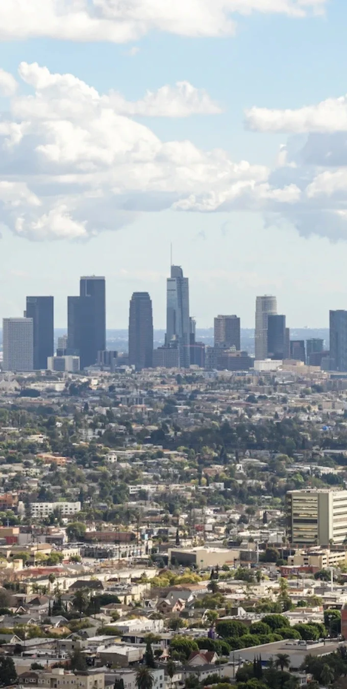 Horizonte del centro de Los Ángeles al fondo, con cielos azul intenso y nubes al frente, y otros vecindarios de LA en primer plano.